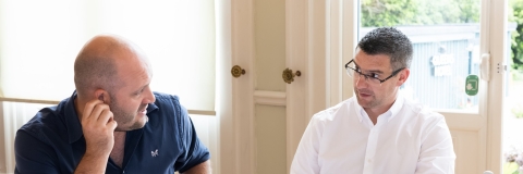Two men at a table with their laptops talking