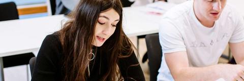 Female student seated next to male student reading a book