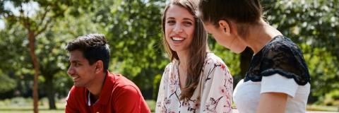 Three students, sitting on a bench in a park, talking and laughing