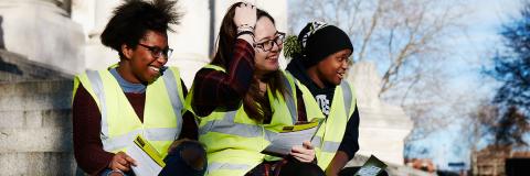 Three students sat on the steps of Guildhall, wearing high visibility jackets