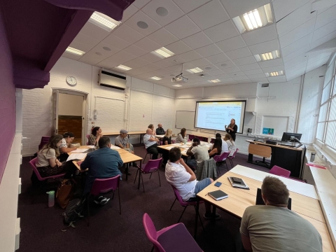 A group of people seated at tables in a classroom, engaged in discussion and collaborative activities.
