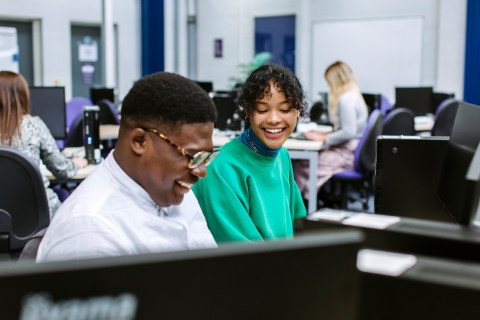 Two students laughing sat in front of a computer