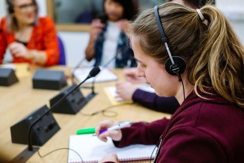 Student in headset takes notes at table in interpreter suite