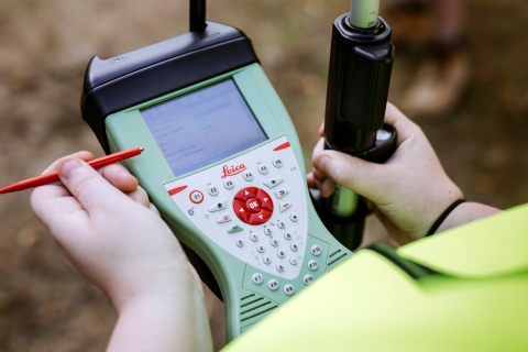Student kneels next to the drone taking readings on touchpad outside Technology Facilities