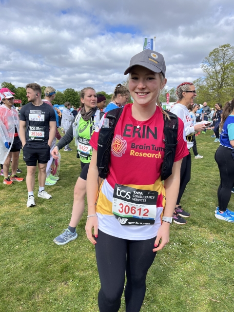 Erin smiling to a camera at a marathon event wearing a hat and running gear with a label saying she is raising funds for Brain Tumour Research.