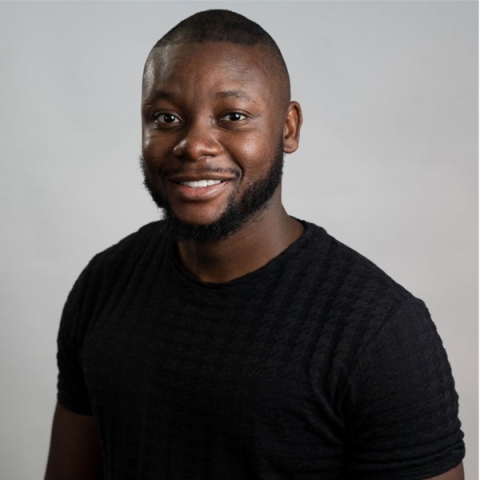 Alumnus Joel Beya smiling to camera wearing t-shirt