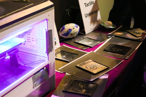 An exhibition table displaying 3D-printed tactile graphics of galaxies and astronomical objects