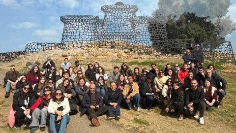 A  picture of the students on the workshop in front of one of the ruins of the Nuraghe of Genna Maria in Villanovaforru. Overlaying the ruins is a depiction of what the monument would have looked like originally 