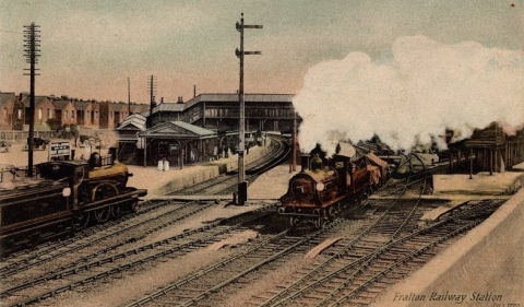 A colourised old photo of Fratton train station with a two steam trains and the station itself