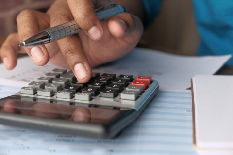Close up of a hand holding a pen and using a calculator