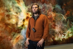 Dr Nicolas Bonne against a backdrop featuring a Hubble Space Telescope image of a small section  of the Carina Nebula - a vast cloud of dust and gas that contains  thousands of stars
