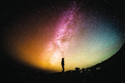Image of a twilight sky with the silhouette of an individual in the foreground, standing in a field or park