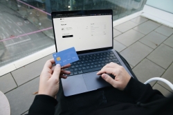 Image shows someone using a laptop and holding a debit or credit card as if purchasing an online product or service