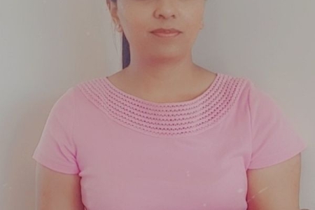 Female with dark hair tied back wearing a pale pink short sleeved top starting at the camera