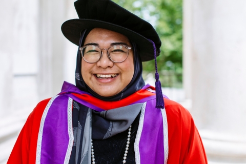 A postgraduate research student smiling in her graduation attire