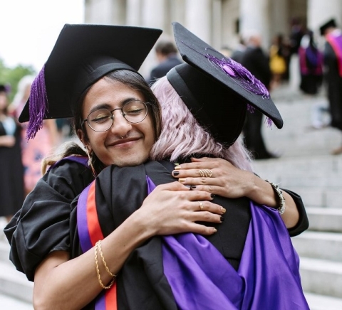 Graduates hugging each other wearing academic dress