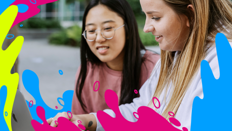 Two students are looking at a laptop screen together, displaying interest and collaboration in their task.